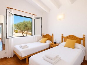 Een hotelkamer met twee bedden, een groot raam met gordijnen, een nachtkastje en een wandlamp.