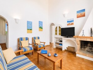 Een woonkamer met een bank, twee gestreepte fauteuils, een salontafel, een televisie en een open haard.