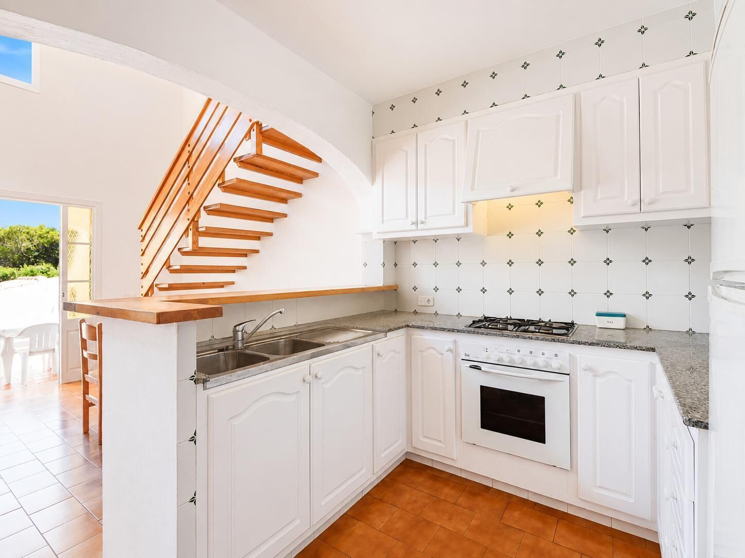 Una cocina con armarios blancos, una escalera de madera, una estufa a gas y un lavamanos.