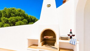 Een buitenkeuken met een pizzaoven, een barbecue en wijnglazen.