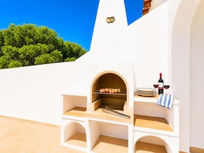An outdoor kitchen with a pizza oven, a grill, and wine glasses.