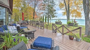 Une terrasse en bois, meublée pour l’extérieur, agrémentée de plantes en pot et offrant une vue sur un lac.