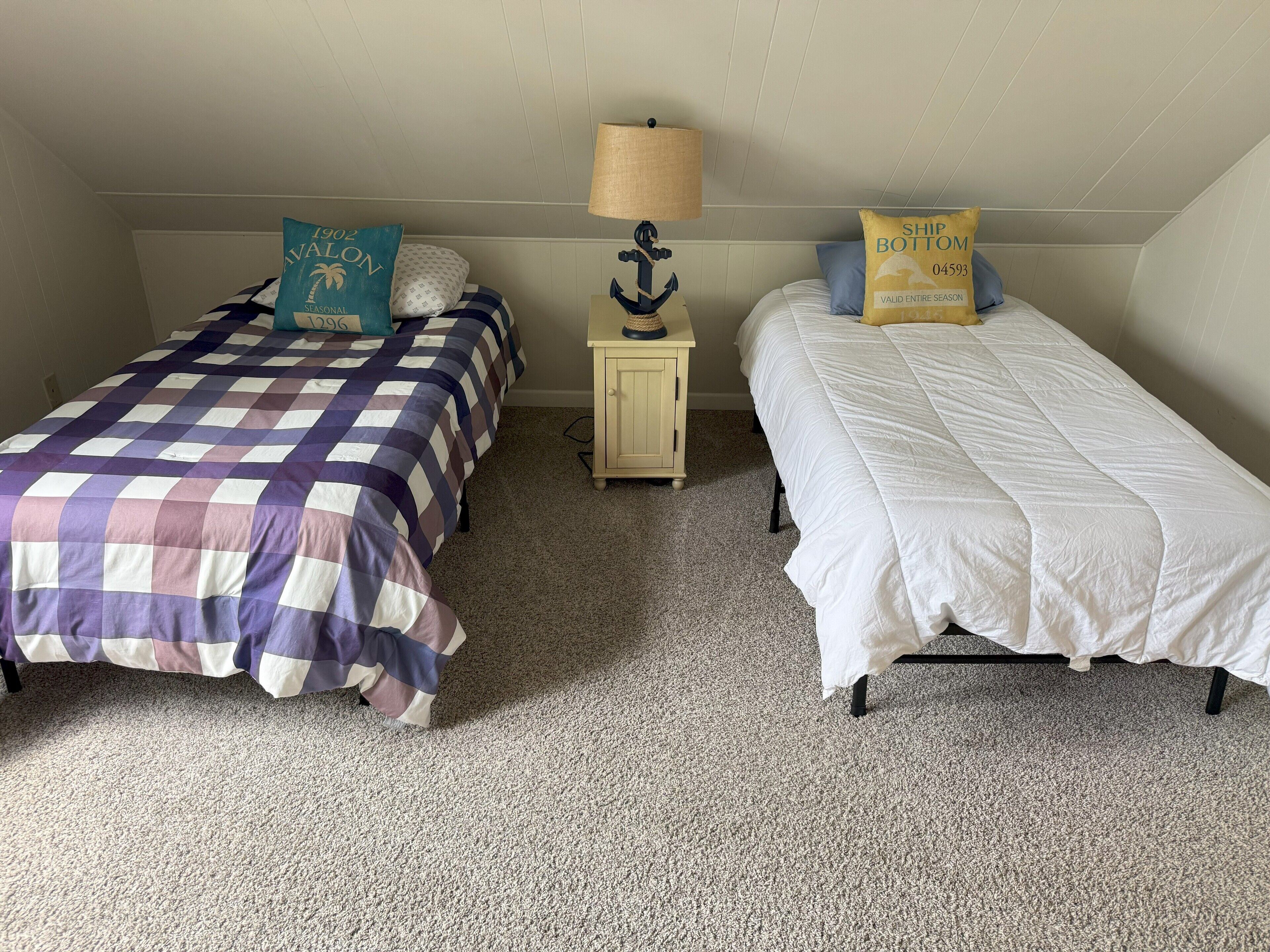 A bedroom with two beds, each with a different patterned bedspread. There is a small wooden nightstand with a lamp between the beds.