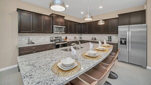 A modern kitchen with dark cabinets, a granite countertop, stainless steel appliances, and pendant lighting.