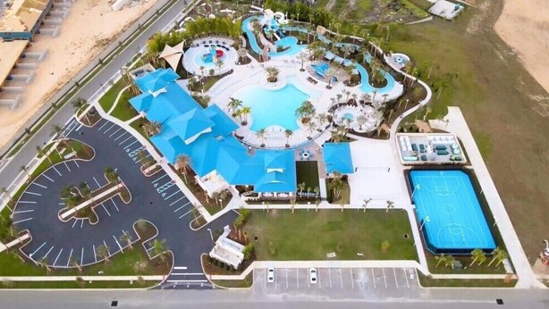 An aerial view of a resort with a large swimming pool, a basketball court, and a parking area.