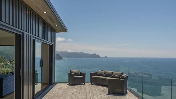 A balcony with a wooden floor and two wicker sofas facing a scenic ocean view.