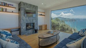 A modern living room with a stone fireplace, a large window overlooking a scenic view, and a chessboard on the coffee table.