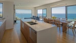 A modern kitchen with a large island, wooden cabinets, and a view of the sea.