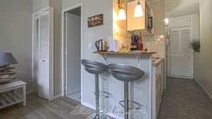 A compact kitchen with a bar stool, a kettle, a toaster, and a red appliance on the counter.