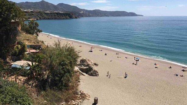 A beach with clear blue water, sandy shore, and mountains in the background. - SHR002 Nuevo y Moderno apartamento en Nerja con Patio (Nerja)