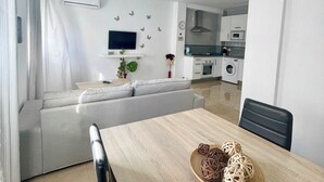 A modern living room with a sofa, a dining table with a bowl of decorative items, and a kitchen in the background. - SHR002 Nuevo y Moderno apartamento en Nerja con Patio (Nerja)
