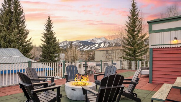 Un patio con sillas Adirondack, un hogar para fuego y vistas a las montañas.