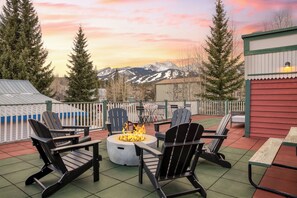 Un patio con sillas Adirondack, un hogar para fuego y vistas a las montañas.