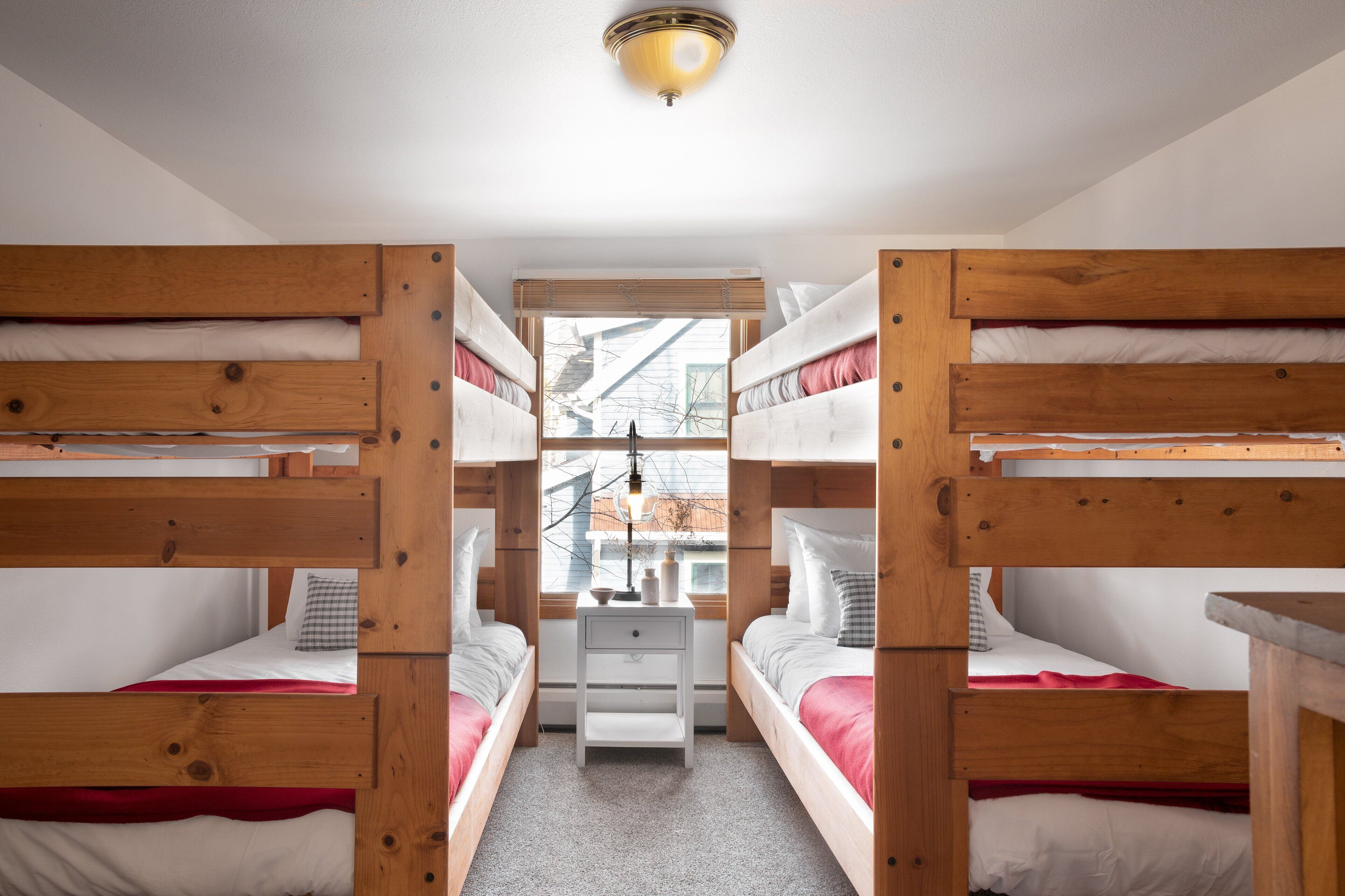 Een kamer met stapelbedden, een klein wit nachtkastje en een raam met uitzicht op gebouwen.