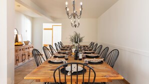 Comedor con una mesa de madera dispuesta para seis comensales, rodeada de sillas negras. Un candelabro cuelga del techo y hay una planta en el centro de la mesa.