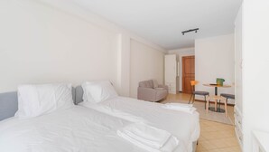 Et hotelværelse med to senge, et lille siddeområde med et bord og stole, samt en dør der fører til et andet værelse.