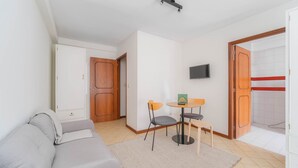 En kompakt opholdsstue med sofa, et lille spisebord med stole, et fjernsyn ophængt på væggen og et skab.