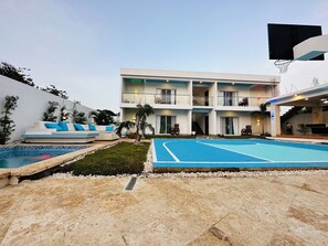 Un edificio moderno de varios pisos con piscina, zona de estar al aire libre y cancha de baloncesto.