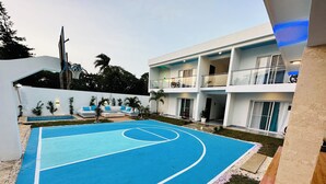 Ein Basketballfeld mit Pool und Lounge-Bereich, umgeben von einem modernen Gebäude mit Balkonen.