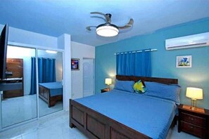 Un dormitorio con una cama, mesitas de noche, ventilador de techo y aire acondicionado.