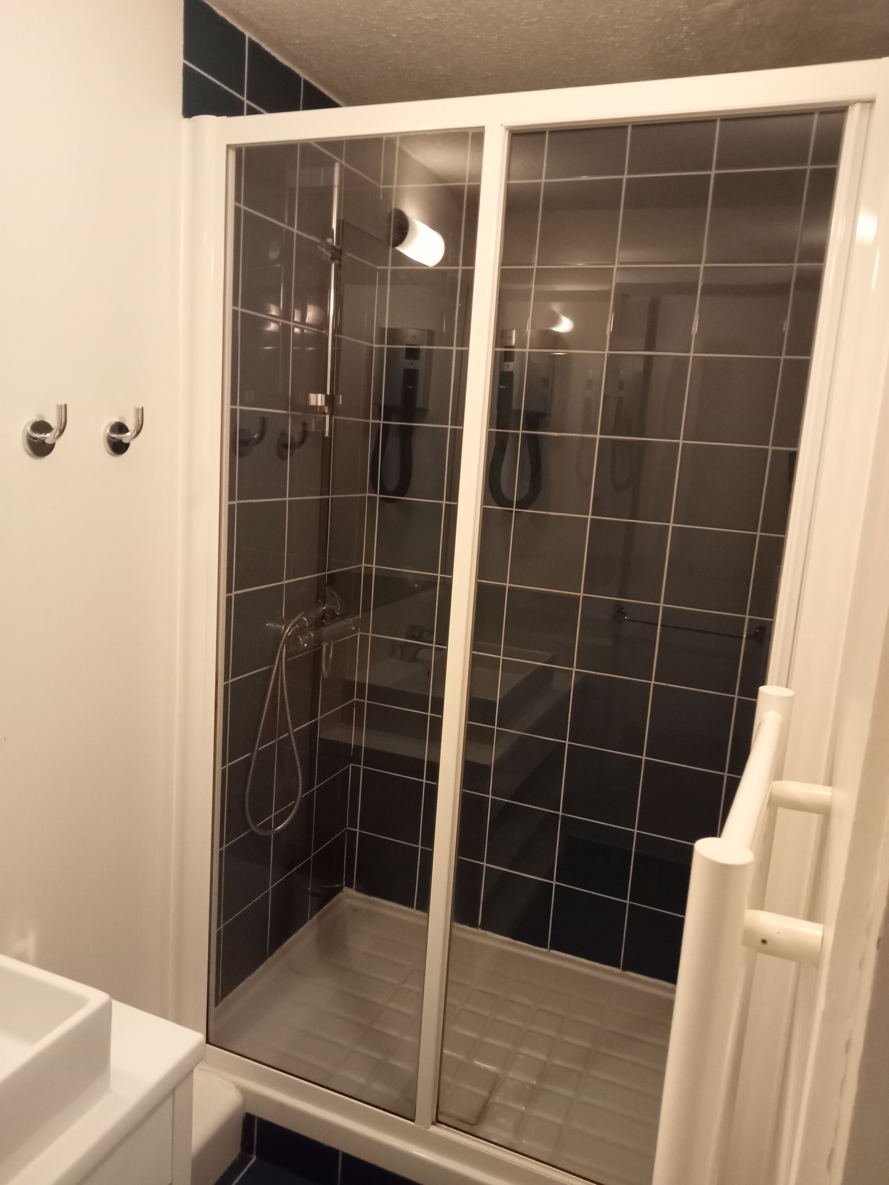 Una ducha sin plato con puerta de vidrio, un lavabo blanco y suelo de baldosas.