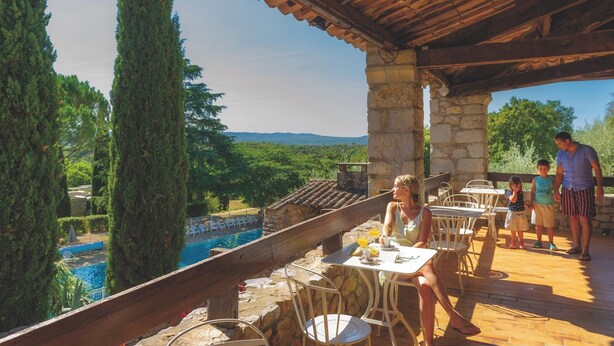 Eine Terrasse mit steinernen Säulen, Sitzgelegenheiten im Freien und Blick auf ein Schwimmbad.