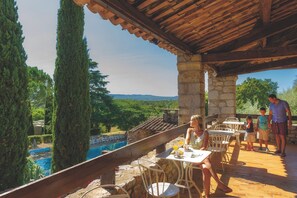 Une terrasse avec des piliers en pierre, des sièges extérieurs et une vue sur une piscine.