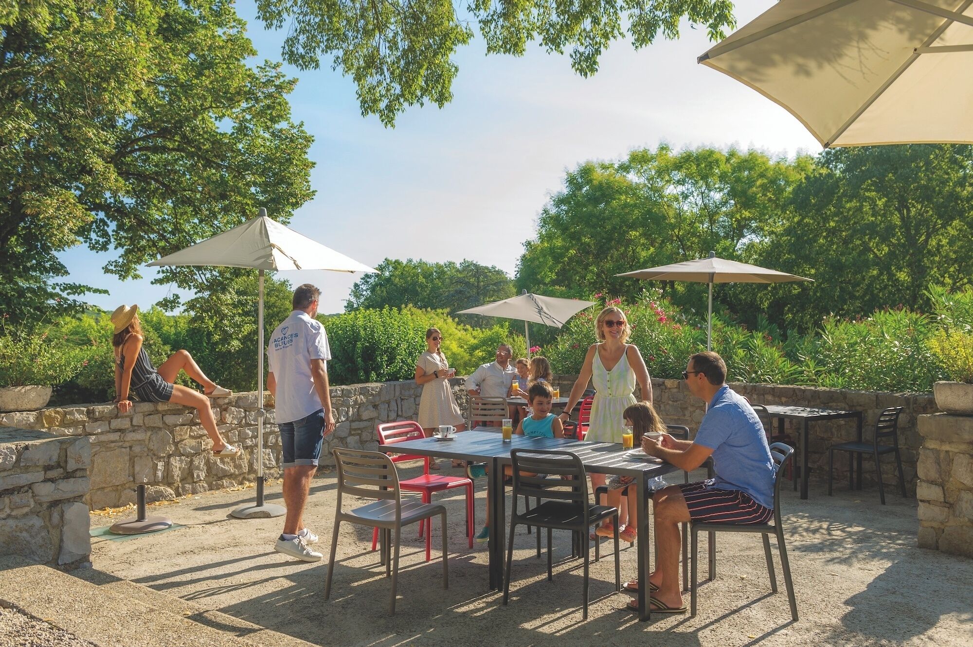 An outdoor patio with stone walls, tables, chairs, and umbrellas.