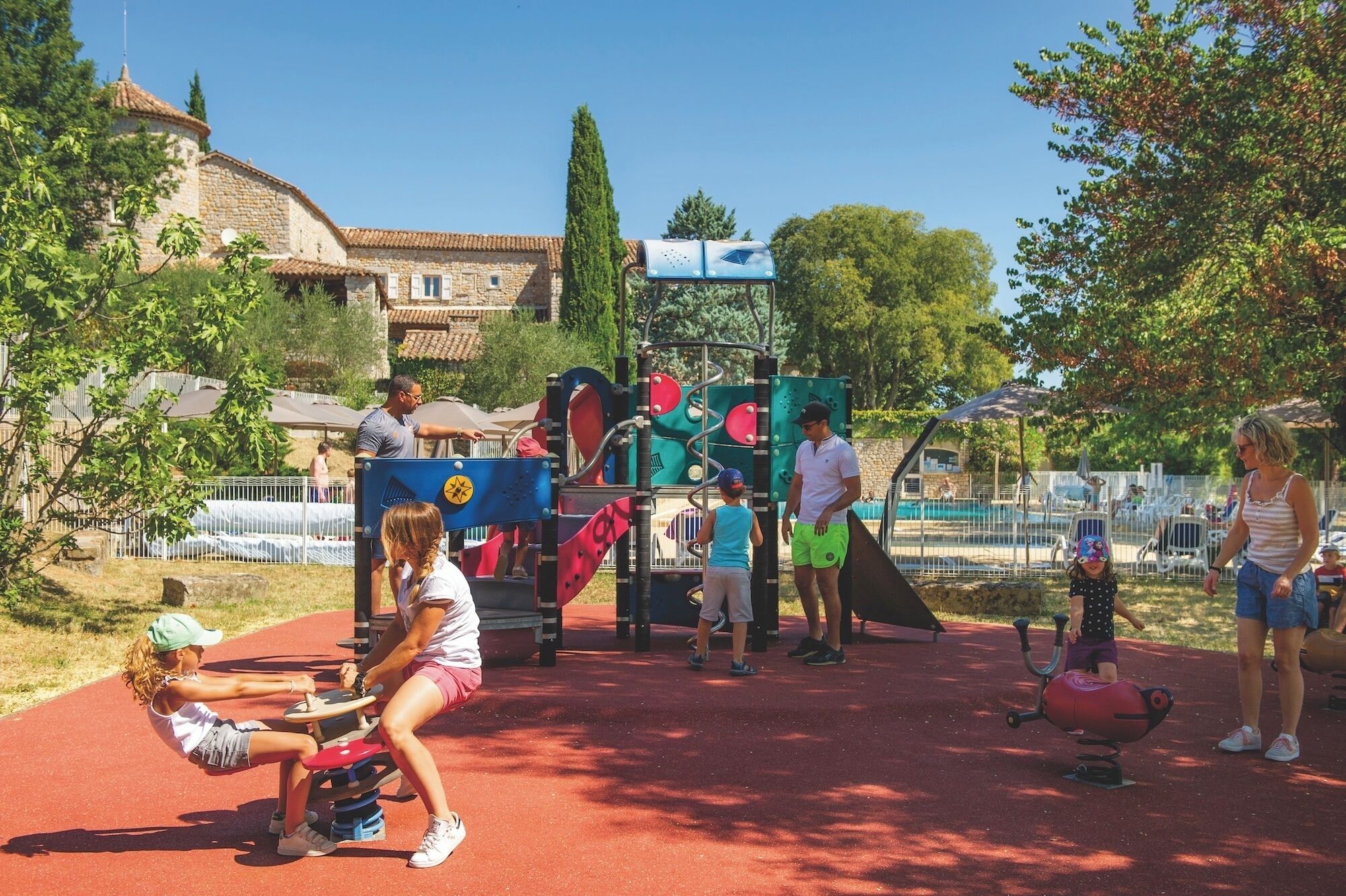 Un parque infantil con equipo de ejercicio, una pista roja y una piscina al fondo.