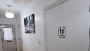Un couloir avec une porte blanche sur laquelle est inscrit le mot « TOILETTES » et un tableau abstrait en noir et blanc accroché au mur.