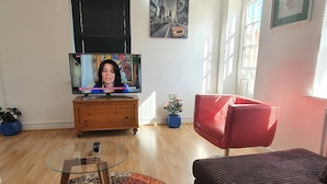 A living room with a television, a red chair, a brown sofa, a glass coffee table, and a patterned rug. - Mannys Apartment - Flagship Lodge (Sittingbourne)