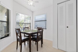 Un coin repas avec une table et des chaises, un ventilateur de plafond et une porte blanche.