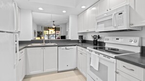 Una cocina moderna con armarios blancos, microondas integrado, estufa y lavavajillas.