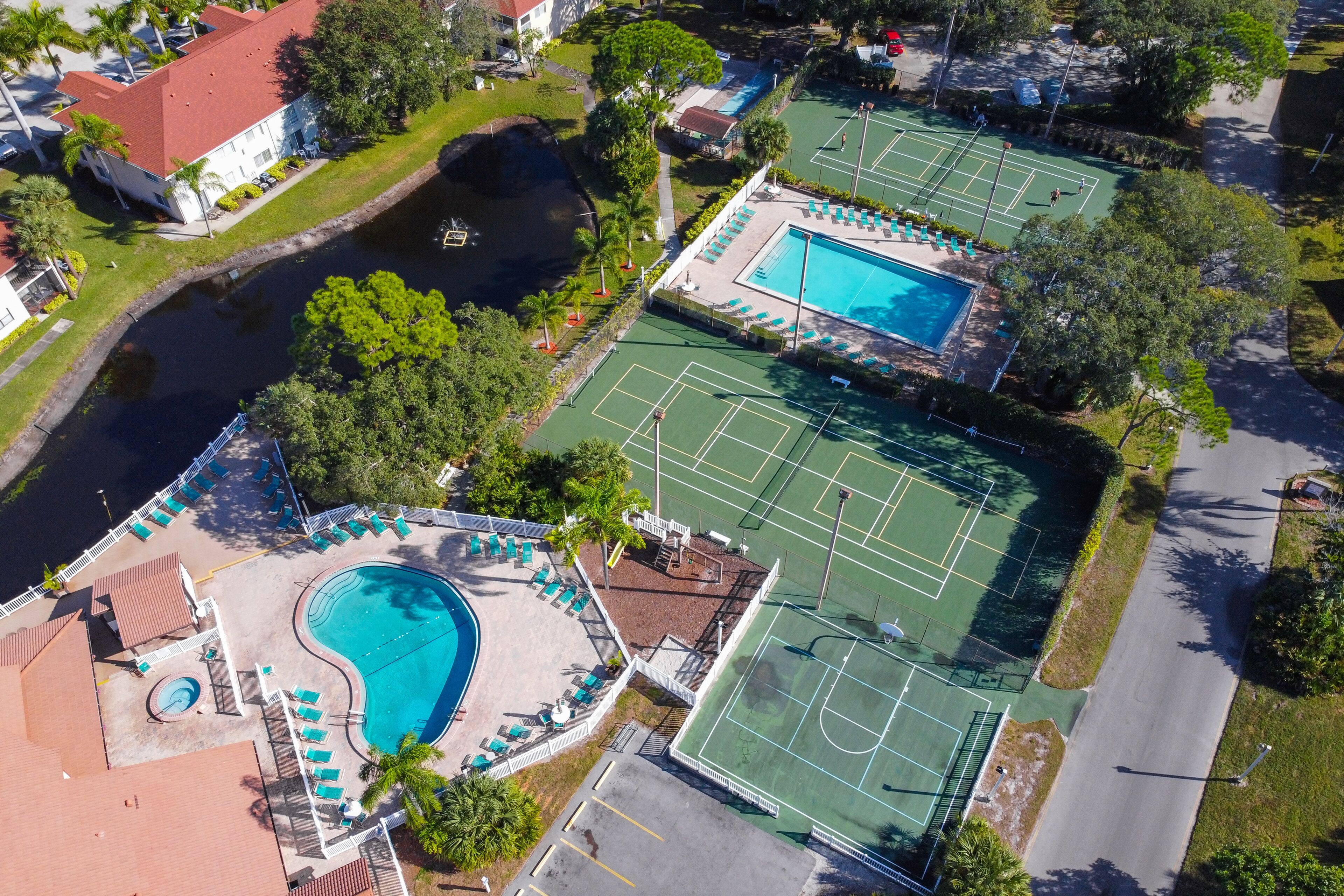 Vista aérea de un complejo turístico con varias canchas de tenis, una piscina y un pequeño muelle junto al agua.