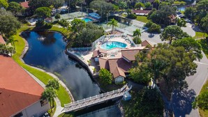 Vista aérea de una zona residencial con piscina, puente y cancha de tenis.
