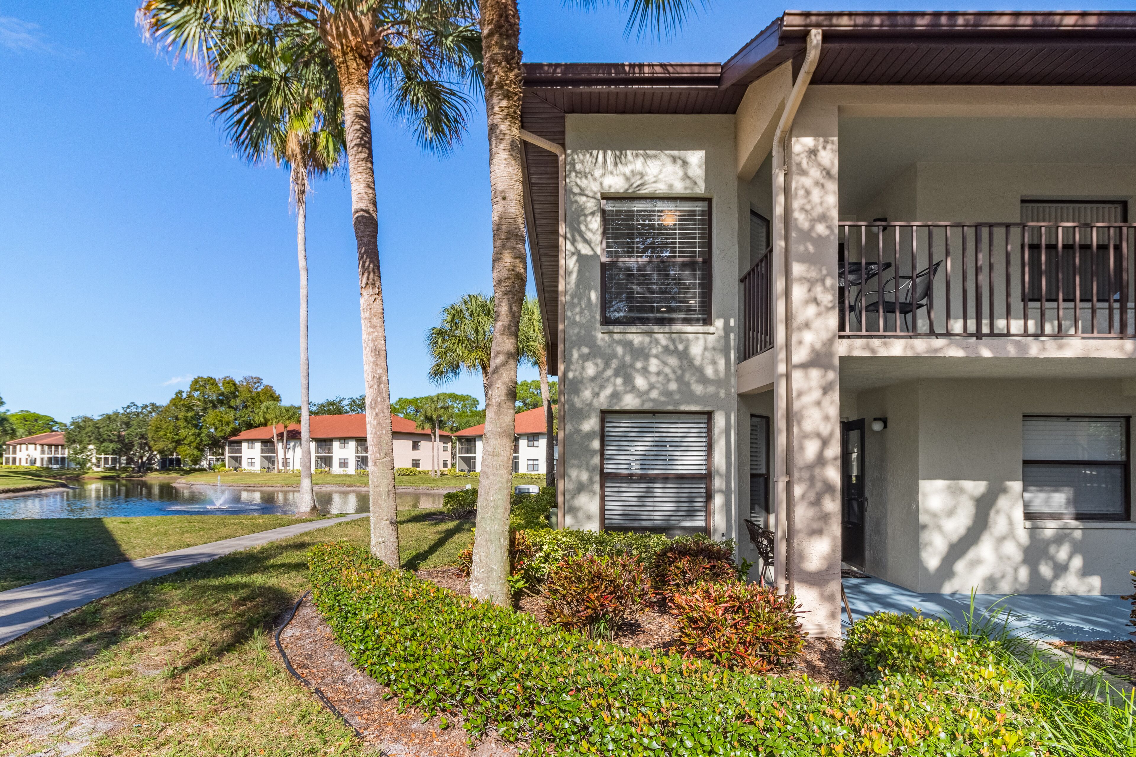 A two-story building with a balcony, a pond, and palm trees.