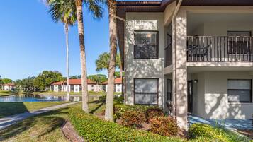 A two-story building with a balcony, a pond, and palm trees.