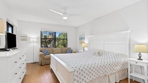 Un dormitorio con cama, televisor, sofá y ventana con vista a la vegetación.