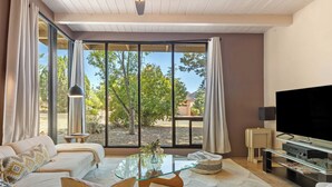 A modern living room with a glass coffee table, sofas, a flat-screen TV, and a view through large sliding glass doors. - Sedona Modern Mid-Century Walk to Hiking Trails, Natural Light, Dinner In The Yard! (Sedona)