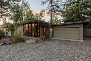 A modern house with a garage, a gravel driveway, and a large tree in front.