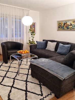 Un salon moderne avec un canapé noir, une table basse en verre, un fauteuil noir et un tapis à motifs.