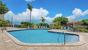 A rectangular swimming pool with a tiled deck, surrounded by lounge chairs and palm trees.