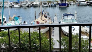 A marina with various boats docked, including sailboats and motorboats, with a view of the sea and distant land.