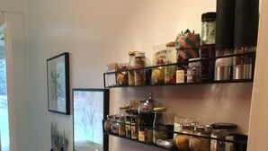 A kitchen with shelves holding jars and spices, a trash bin, and two wooden cutting boards hanging on the wall. - Apartment Château d'Arcadie, 67m2, terrace and garage. The whole of Biarritz on foot! (Biarritz)