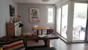 A modern living room with a wooden dining table, a sofa, and a large window offering a view of the outdoors. - Apartment Château d'Arcadie, 67m2, terrace and garage. The whole of Biarritz on foot! (Biarritz)