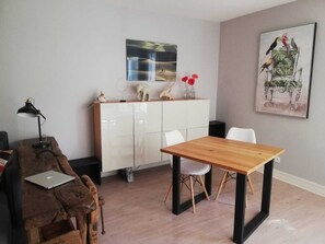 A modern living room with a wooden table, white chairs, a white cabinet, and a painting of birds.