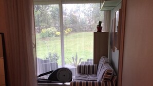 A bedroom with a bed, a striped chair, a small table with a lamp, and a view of a garden through a window. - Apartment Château d'Arcadie, 67m2, terrace and garage. The whole of Biarritz on foot! (Biarritz)