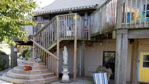 Una terraza de madera con escalones que conducen a un balcón, una estatua y una silla a rayas.
