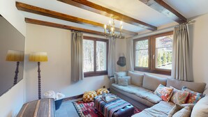 A cozy living room with a sofa, a patterned ottoman, a lamp, and a view of the outdoors through large windows. - Charming Chalet - Walk to Piste & Villars Centre! Style & Comfort 5 Bed/4 Bath! (Ollon)