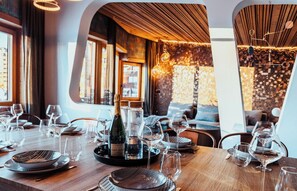 A restaurant interior with a wooden table set for dining, a bottle of champagne, and a mosaic wall in the background. - Immodreams - L'Avorea - Avoriaz (Avoriaz)